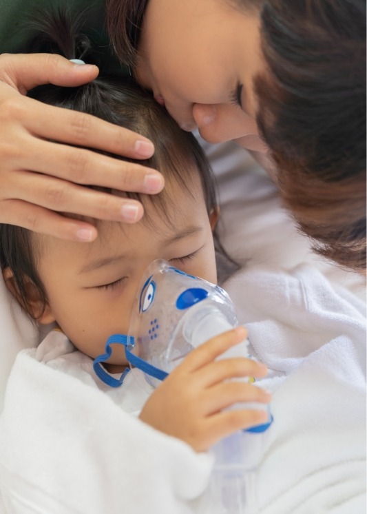 Mother kissing the head of their child in dental chair wearing nasal mask