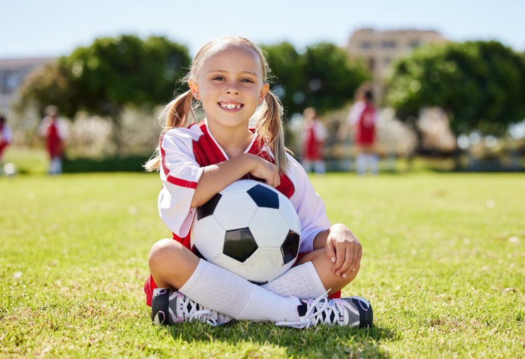 Kid smiles outdoors with soccer ball