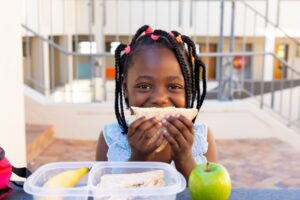a child holding a sandwich up to their mouth while eating at school
